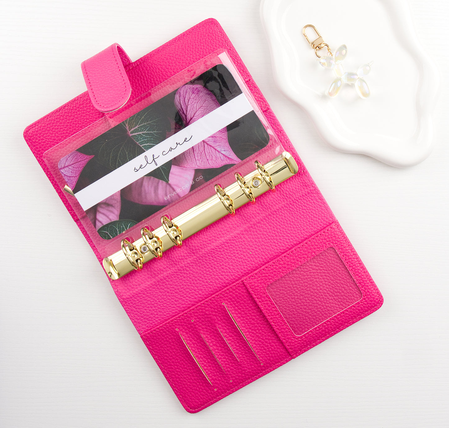 Pink binder with gold binding and leaf designed envelope insert inside all on a white background