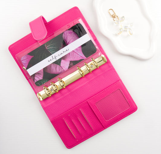 Pink binder with gold binding and leaf designed envelope insert inside all on a white background