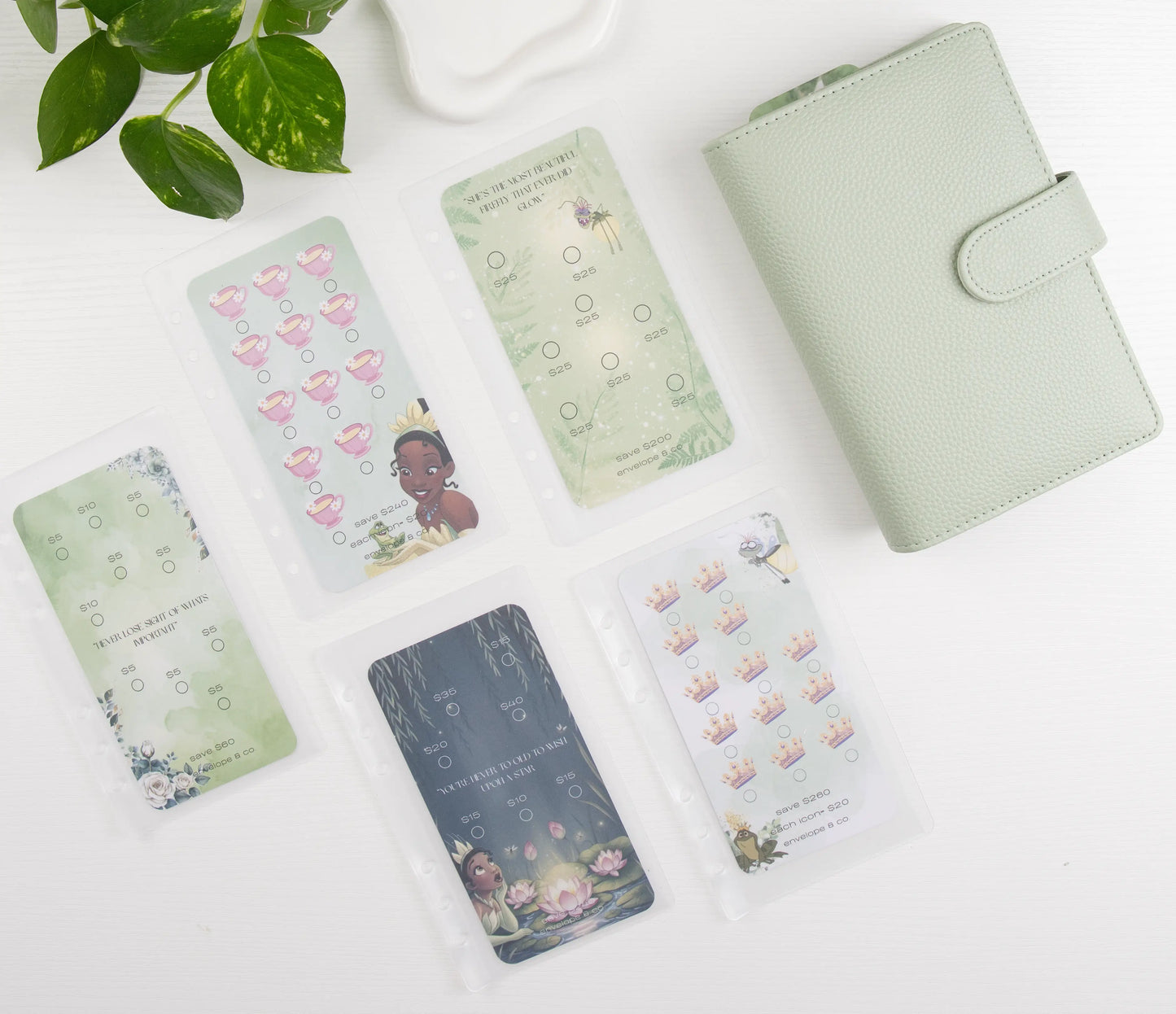 Collection of green savings challenges on a white surface with a plant in the corner.