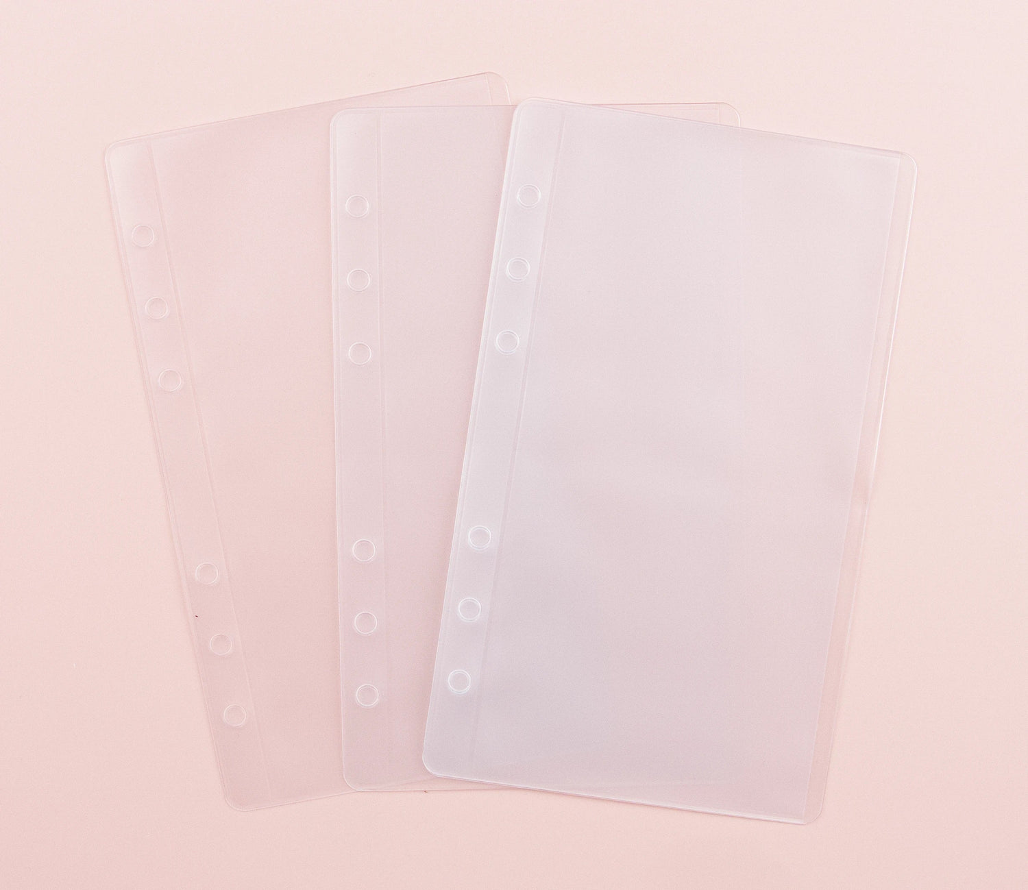 Two clear frosted plastic cash envelopes with 6-hole punch for A6 ring binders, featuring top-loading pocket design, displayed overlapping on blush pink background