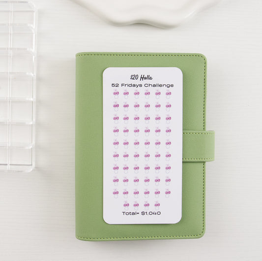 Savings tracker with bows on sage green binder showing 52 weekly milestones.
