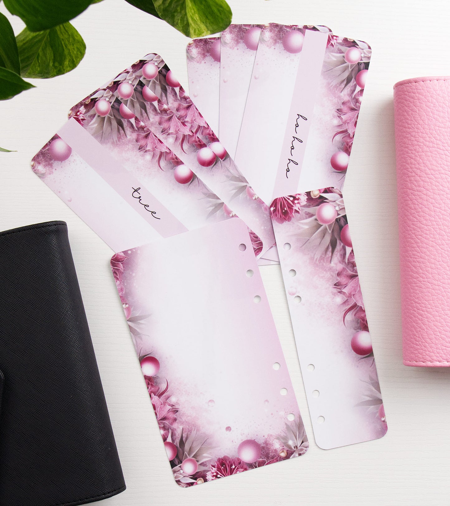 Pink floral and pearl-patterned envelope inserts fanned out on a white surface, with a black binder on the left and a pink binder on the right.