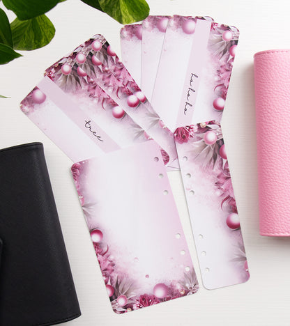 Pink floral and pearl-patterned envelope inserts fanned out on a white surface, with a black binder on the left and a pink binder on the right.