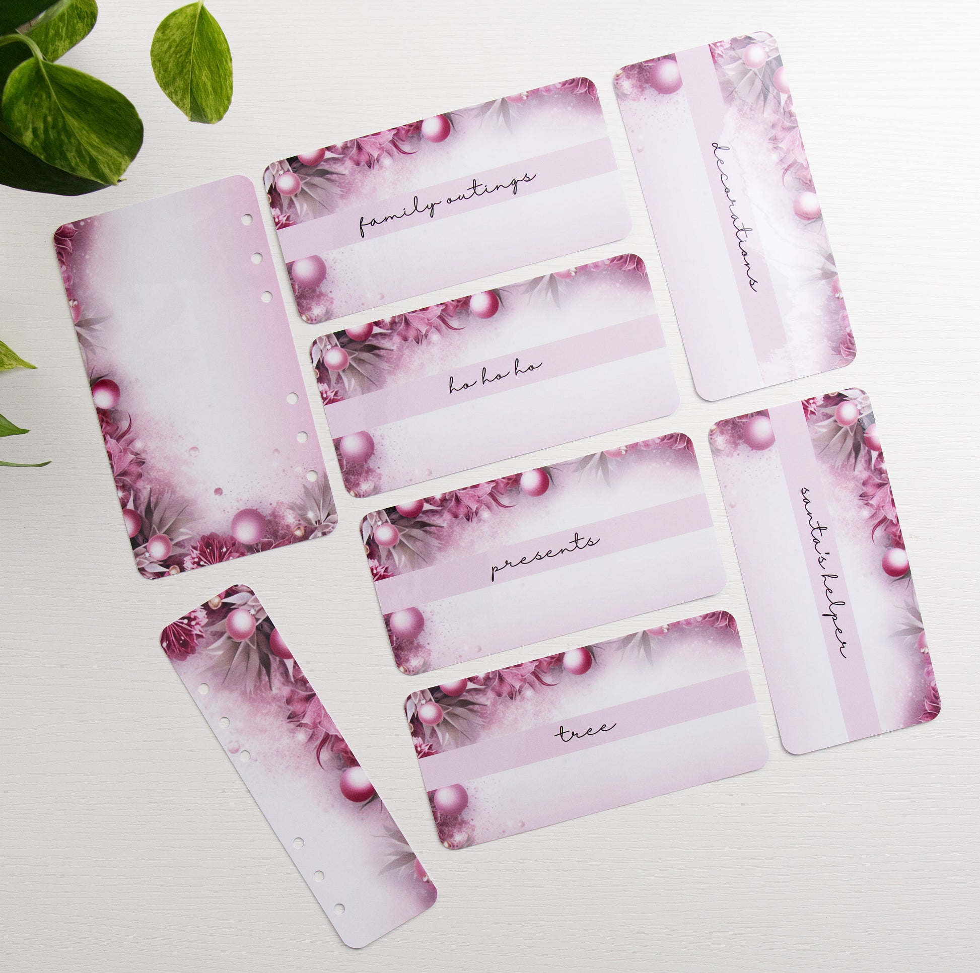 A set of premade, hole-punched savings challenge bundle with a pink and purple winter design, arranged on a white surface with green leaves in the corner.