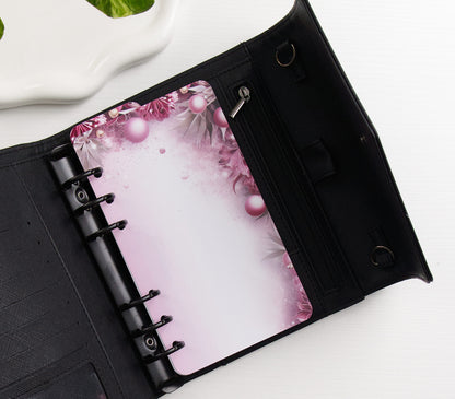 A black ring binder shown open on a white surface, featuring a pink floral and pearl-patterned dashboard page.