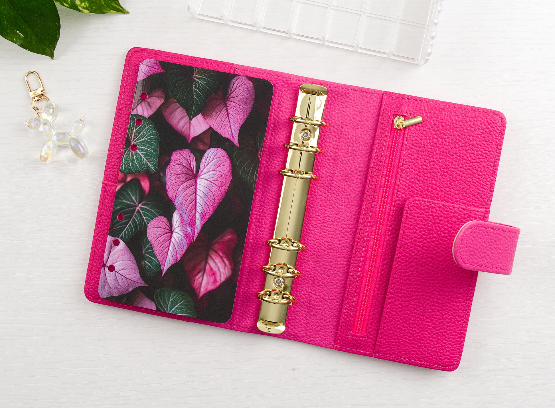 Pink binder with floral design and gold charm on a white background