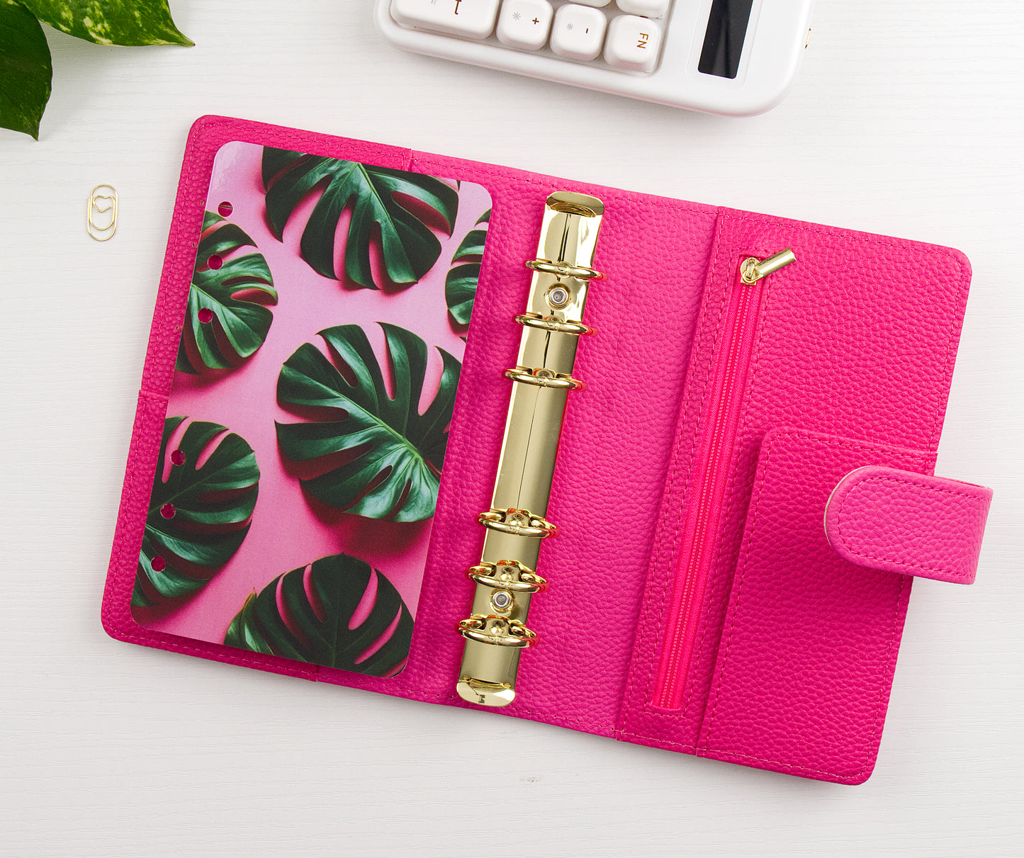 Pink binder with tropical leaf design and gold charm on a white surface