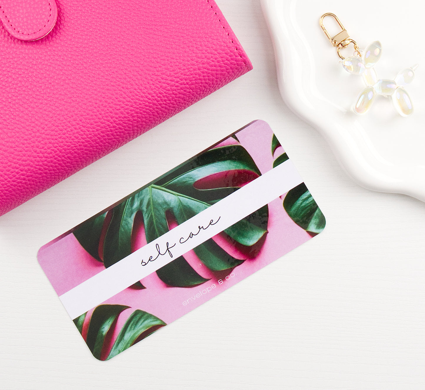 Pink binder with green leaf pattern envelope insert on a white surface with a pink wallet and keychain.