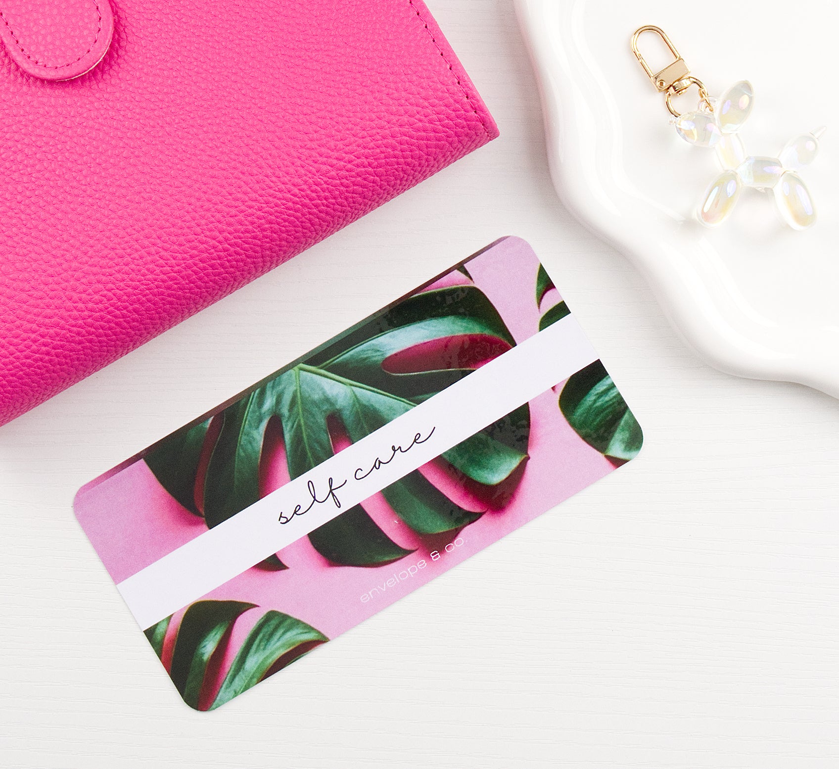 Pink binder with green leaf pattern envelope insert on a white surface with a pink wallet and keychain.