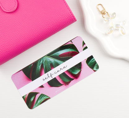 Pink binder with green leaf pattern envelope insert on a white surface with a pink wallet and keychain.