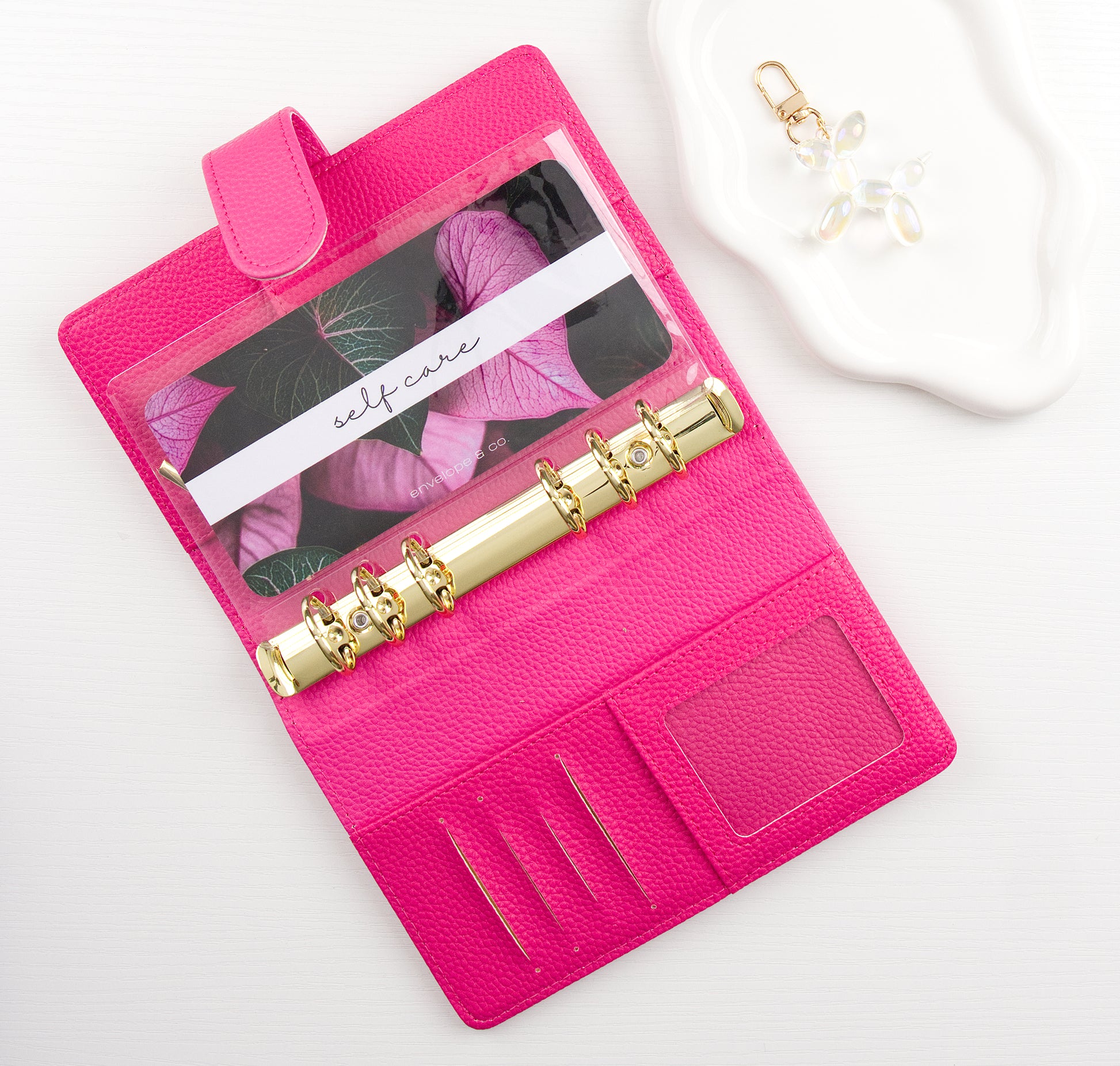 Pink binder with gold binding and leaf designed envelope insert inside all on a white background