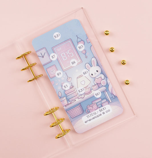 Kawaii savings challenge insert with pastel pink and blue bunny bedroom illustration, dollar amounts $3-$20 scattered throughout cozy scene toward $100 goal, displayed in clear A6 binder with gold rings on pink background