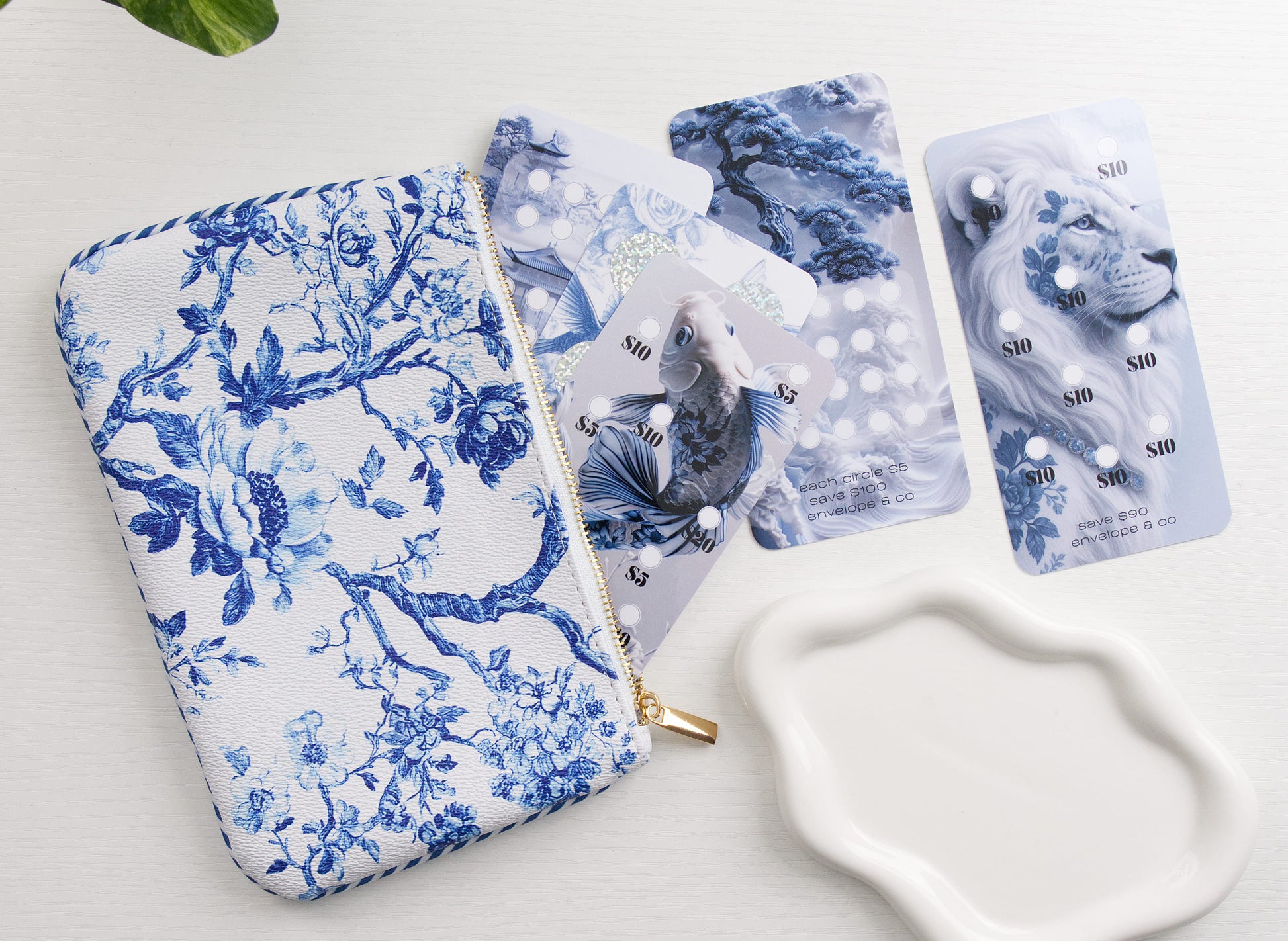 a blue and white patterned cash bag with a blue koi fish and lion themed savings challenges with a white dish in the corner