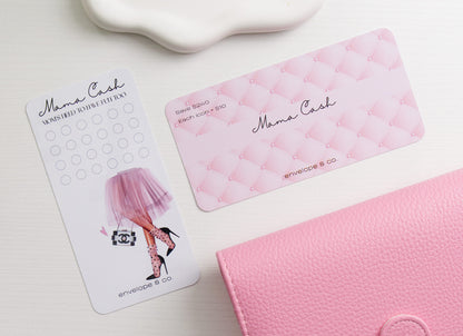 A pink dashboard labeled 'Mama Cash' and a white savings challenge with a fashion illustration arranged on a white surface beside a pink binder.