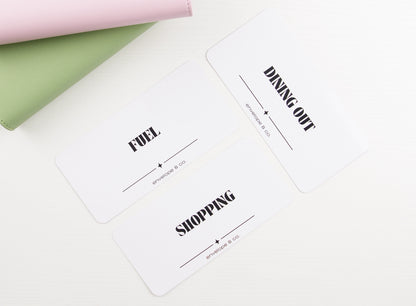 Three minimalist white cash envelope inserts with bold black typography reading Fuel, Dining Out, and Shopping, styled with blush pink and sage green binders on white background