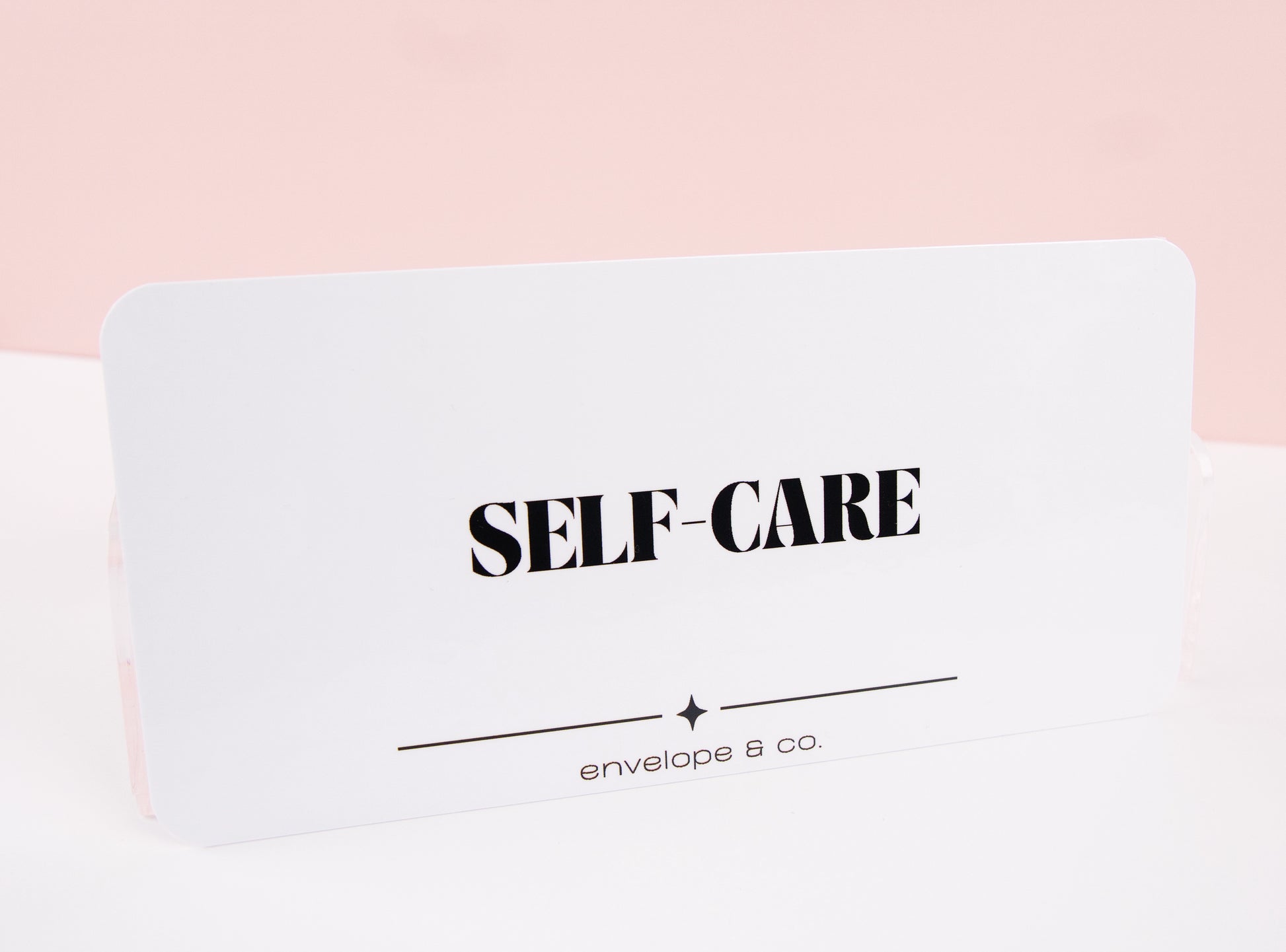 Minimalist white Self-Care cash envelope insert with bold black typography and star accent line, displayed standing against soft pink background