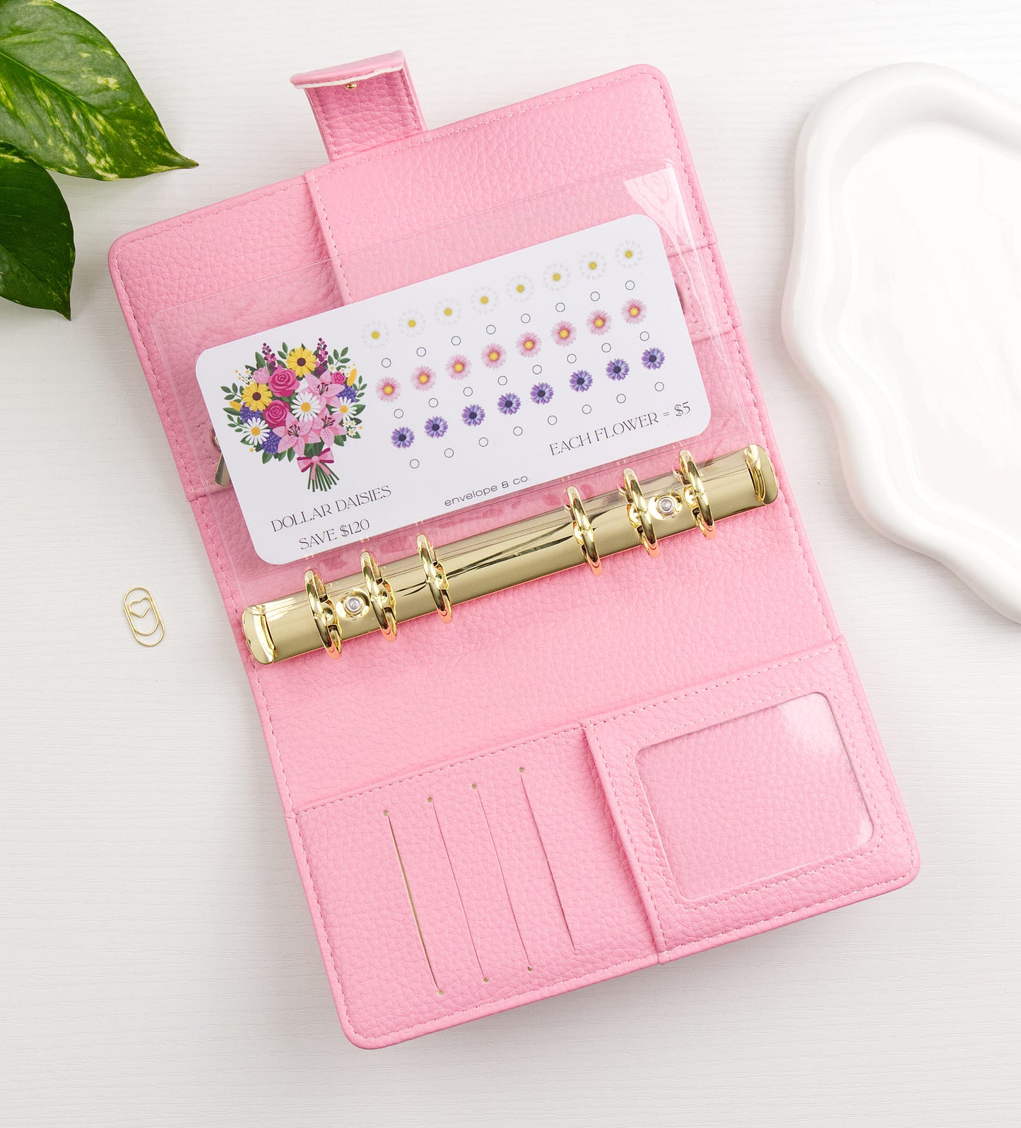 Floral savings challenge in a pink binder with gold clasp on a white surface