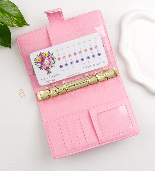 Floral savings challenge in a pink binder with gold clasp on a white surface