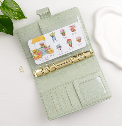 Light green binder with gold rings on a white surface, featuring a savings challenge with floral designs.