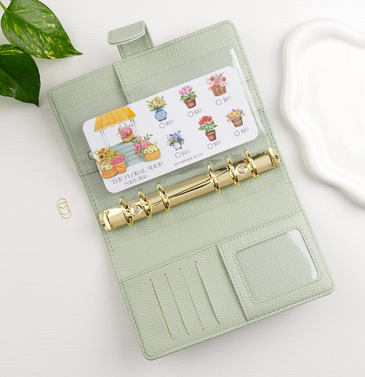 Light green binder with gold rings on a white surface, featuring a savings challenge with floral designs.