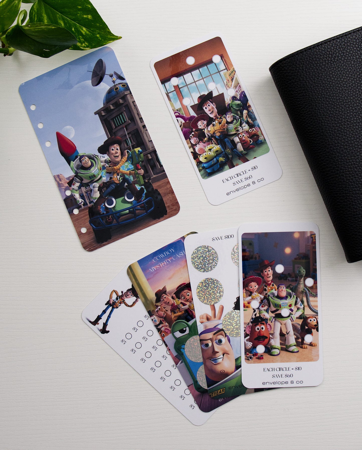 character themed savings challenges on a white background with a black binder and plant in the corners