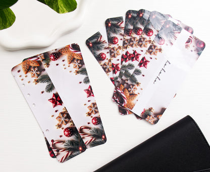 A set of white savings challenge bundle inserts with a festive Christmas print, including pine branches, red ornaments, candy canes, and snowflakes, arranged on a white surface next to a black binder and white dish.
