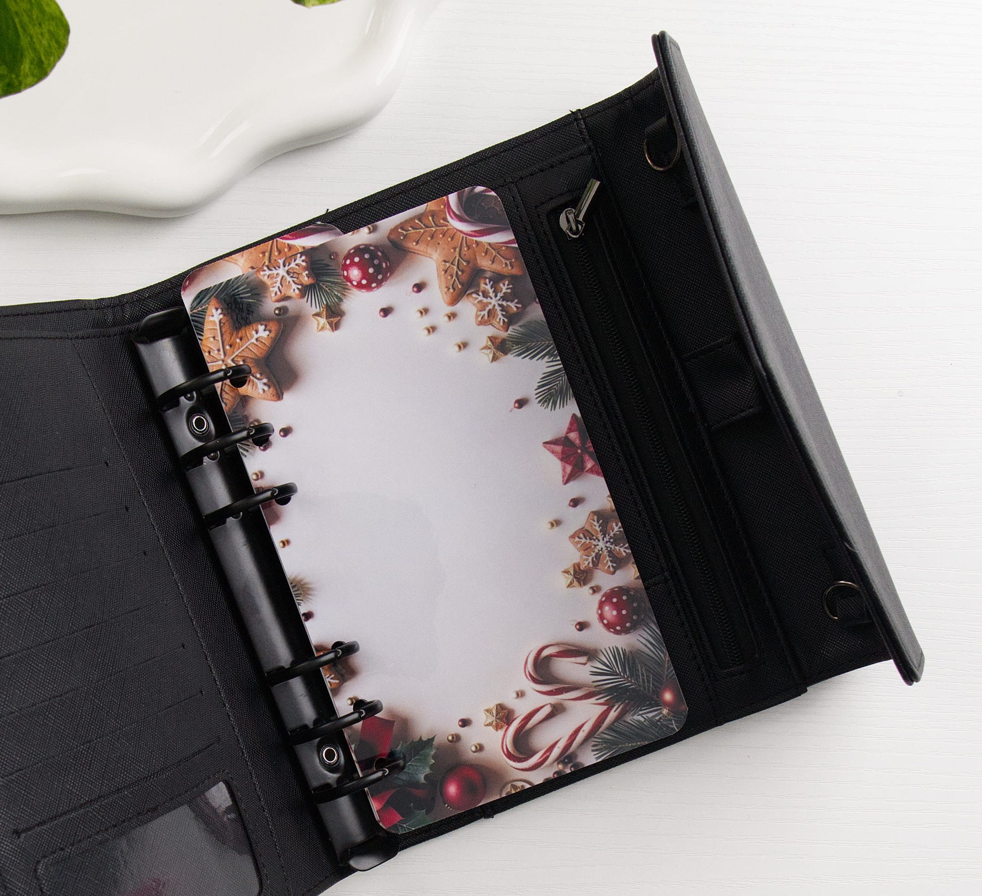 A black binder shown open on a white surface, featuring a festive Christmas-themed printed dashboard with gingerbread cookies, ornaments, candy canes, and pinecones.