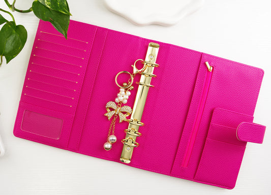 Pink binder with gold binder chain and decorative elements on a white surface