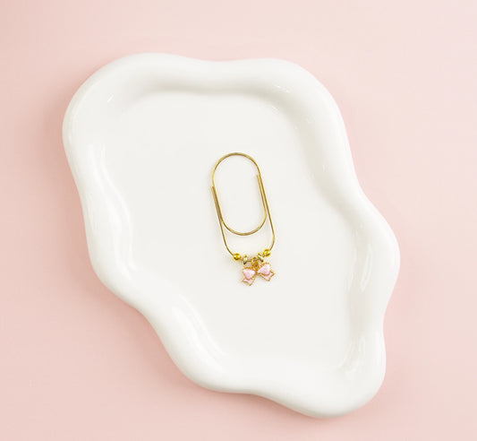 Gold paper clip with pink charms on a white dish against a pink background