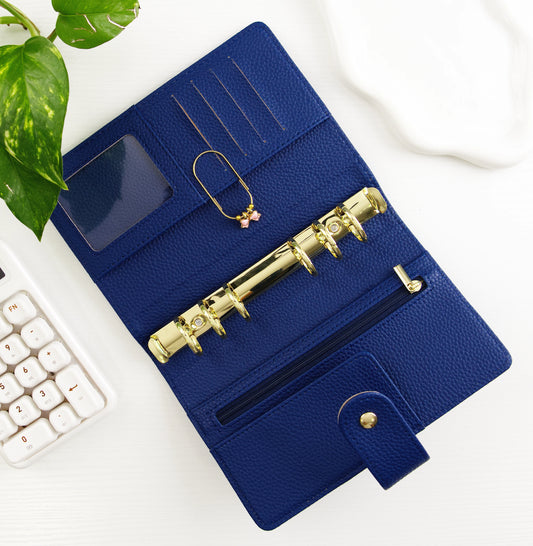 Blue binder with gold accents on a white surface with a plant and calculator in the background