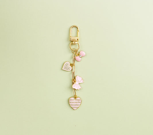 Gold heart-themed charm with pink enamel hearts, displayed against a green background.
