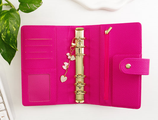 Pink binder with gold binder clip on a white surface with a plant in the corner