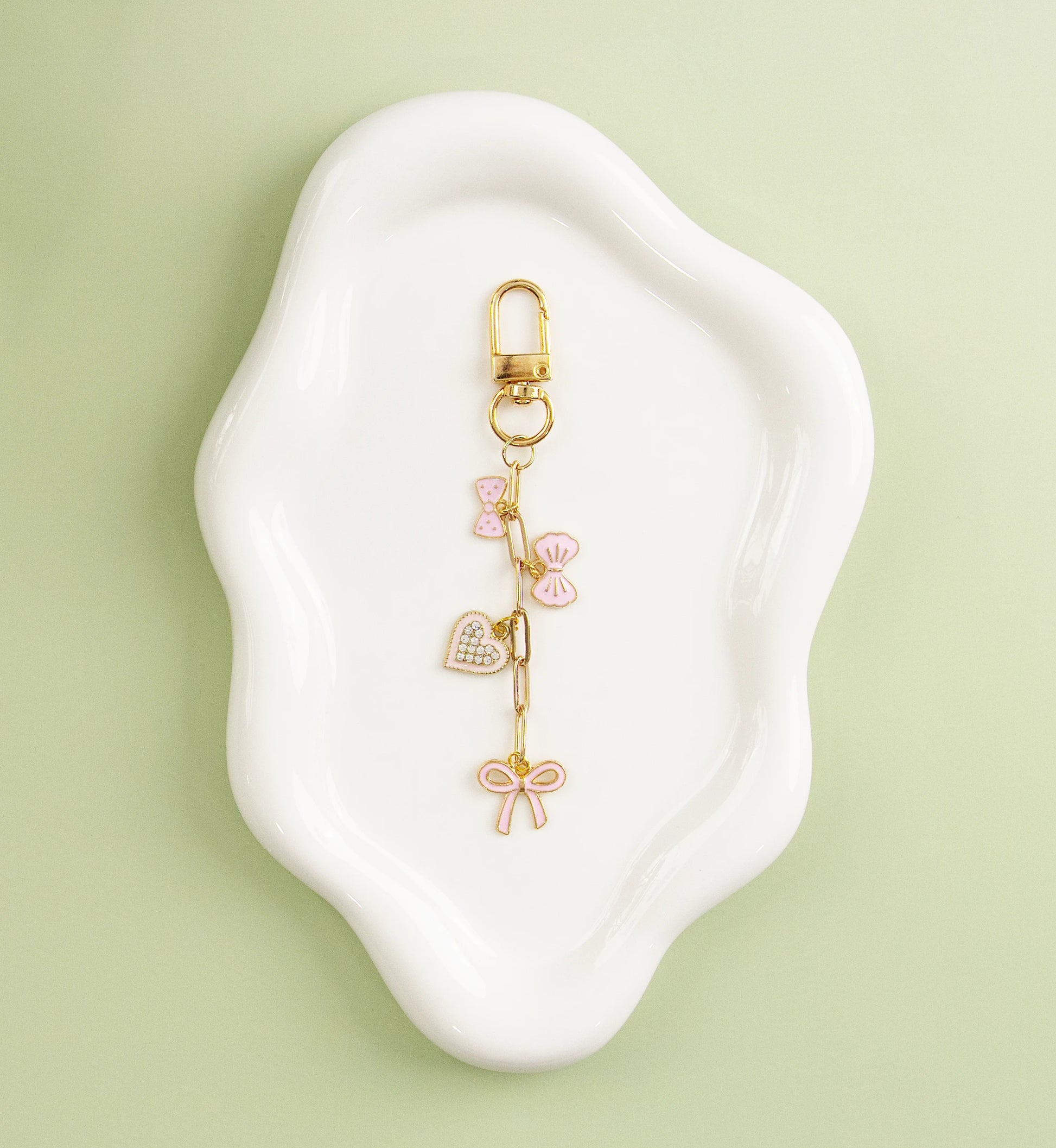 Gold heart-themed charm with pink enamel hearts, displayed on a white dish against a green background.
