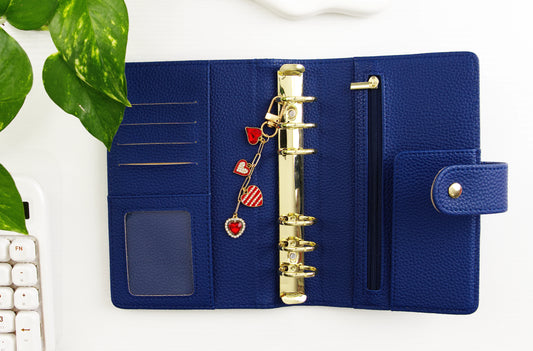 Blue binder with gold rings and heart-shaped charms on a white surface with green leaves.