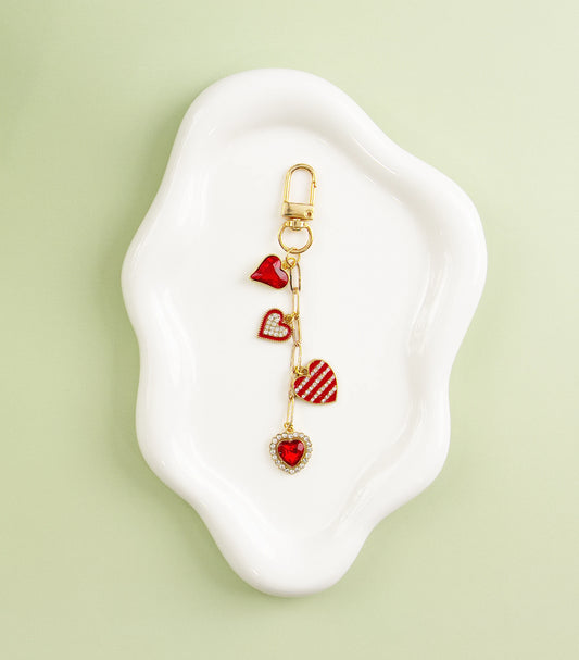Gold heart-themed charm with red enamel hearts, displayed on a white dish against a green background.