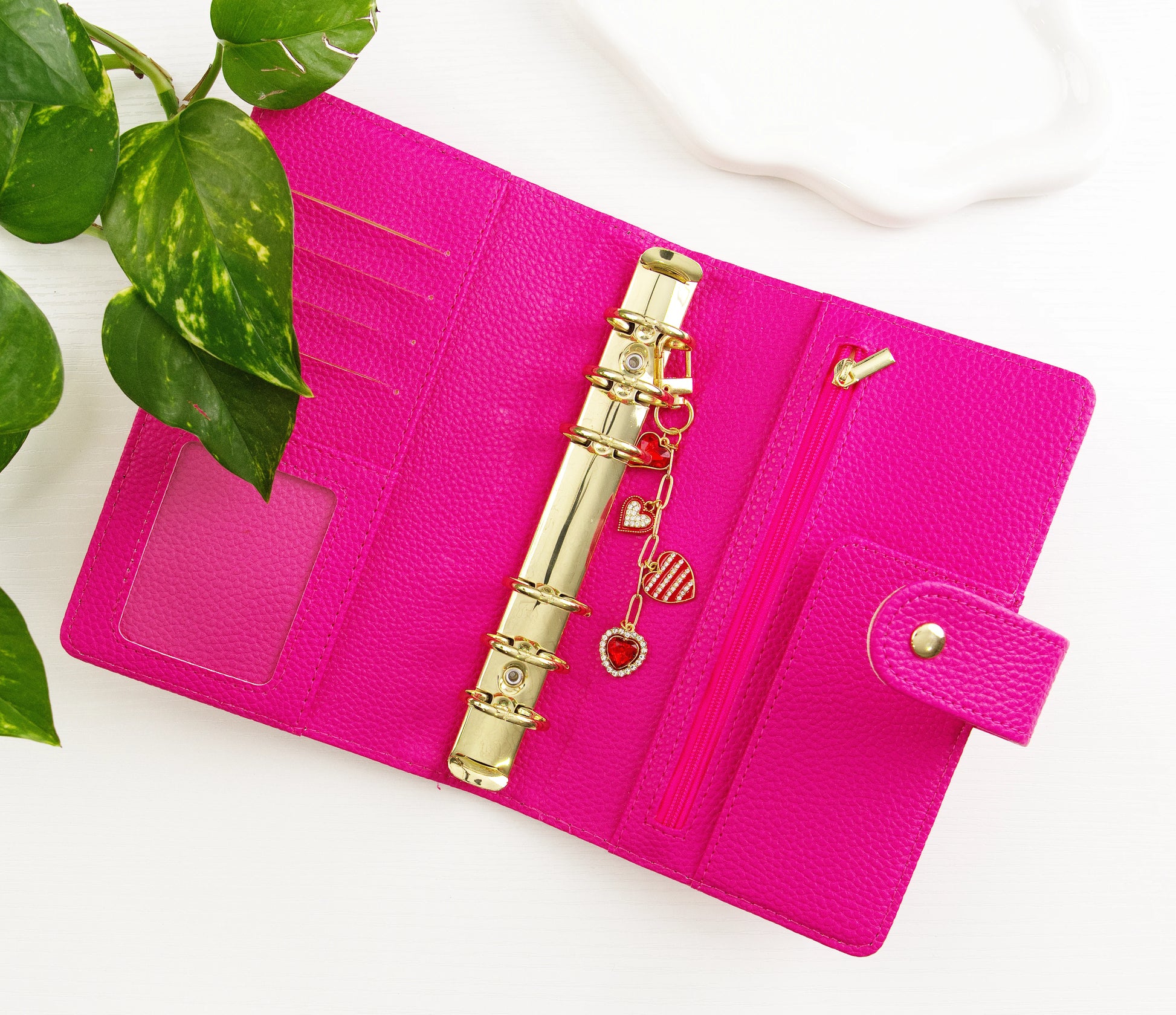 Pink binder with a gold clip and charms on a white background