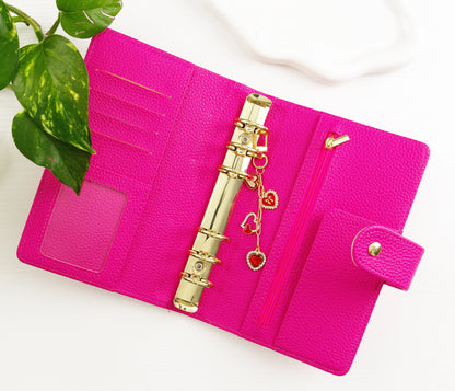 Pink binder with gold ring and gold and red heart charms on a white background