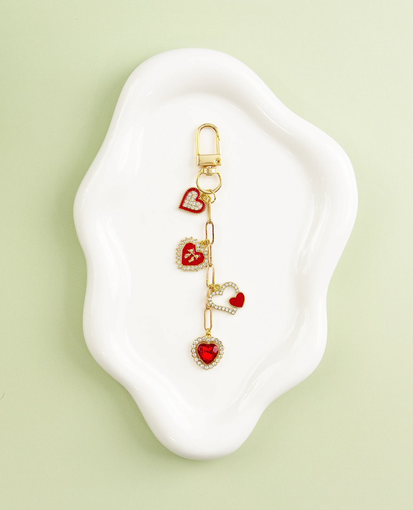 Gold heart-themed charm with red enamel hearts, displayed on a white dish against a green background.