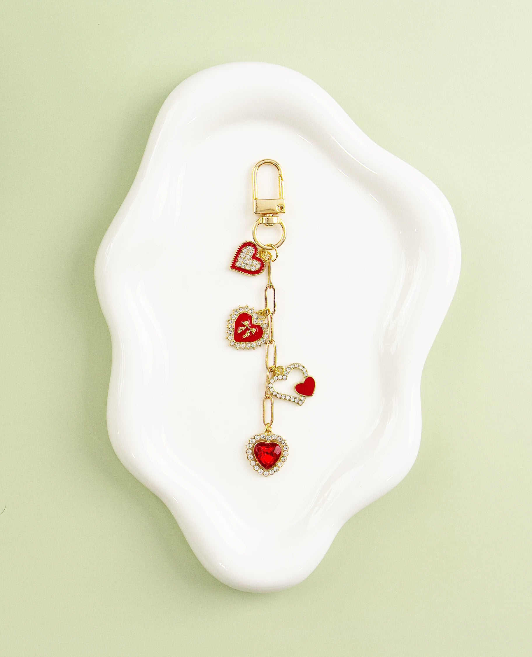 Gold heart-themed charm with red enamel hearts, displayed on a white dish against a green background.