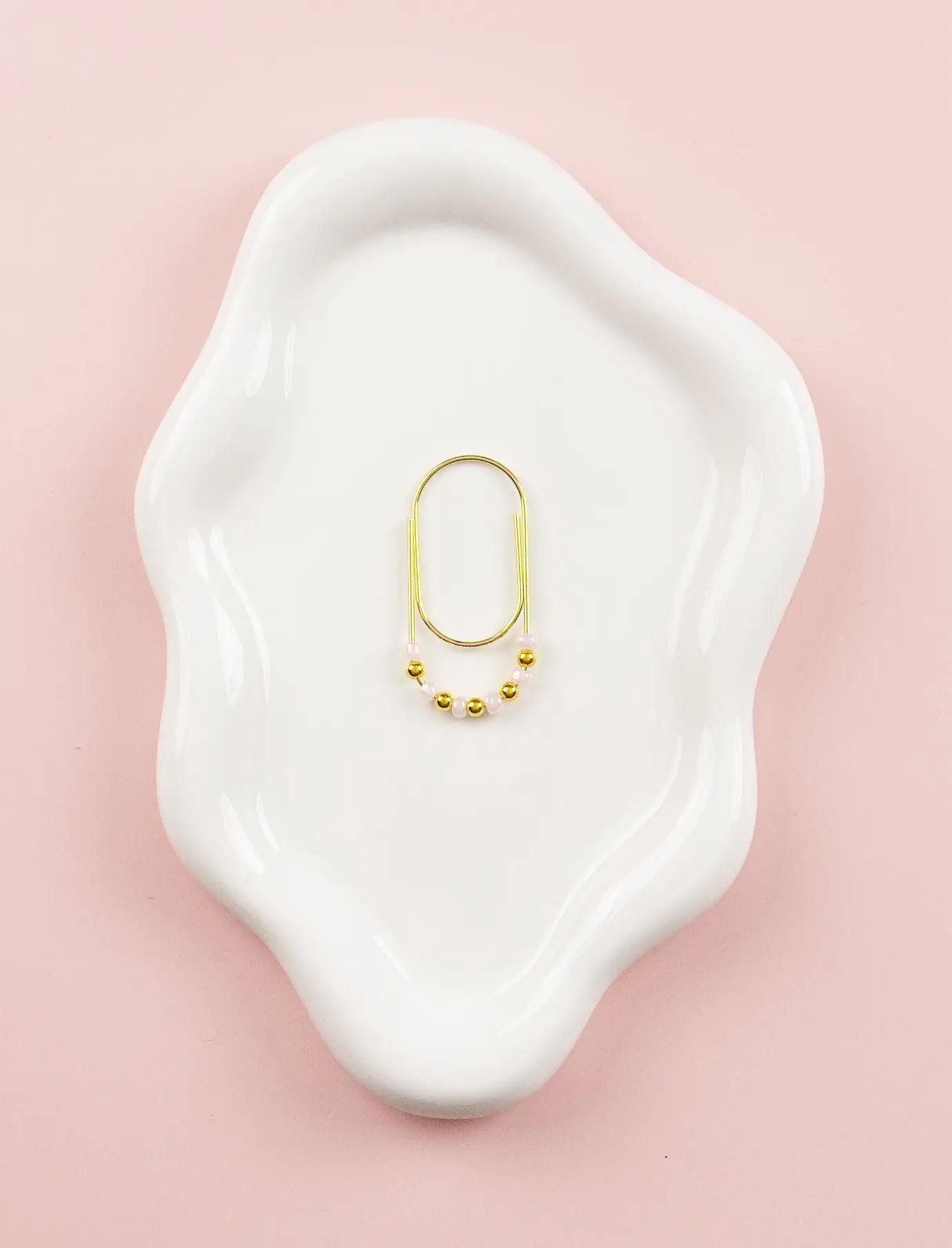 Gold paper clip charm on a white dish with a pink background