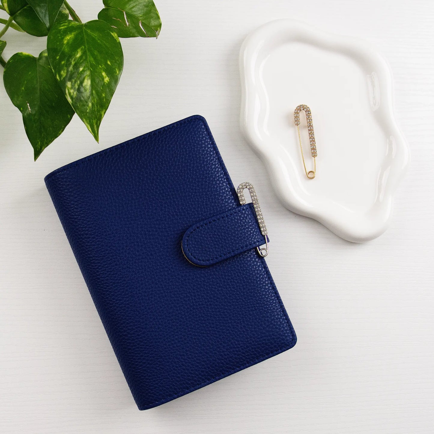 Blue leather binder with decorative clasp on a light surface with a plant and decorative item.