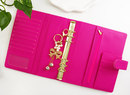 Pink binder with gold binder chain and decorative elements on a white surface