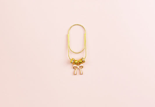 Gold paper clip with small pink bow pendant on a pink background
