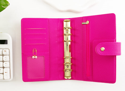 Pink binder with gold binding and a gold paper clip with pink bow charm on a white surface