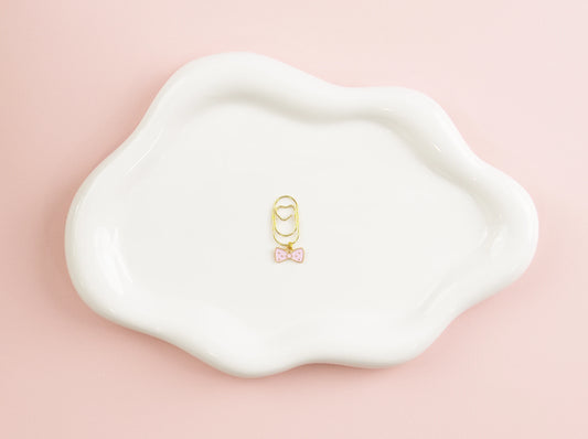Gold bow-shaped charm on a white dish with a pink background