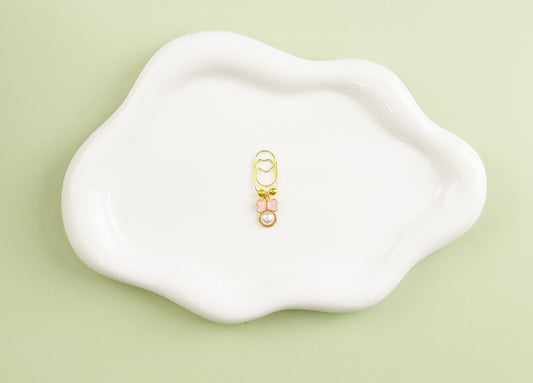 Gold and pink small heart paper clip on a white tray against a light green background