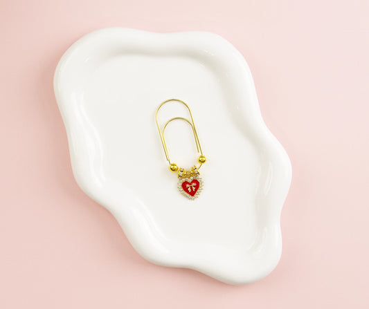 Gold paper clip with a red heart on a white dish against a pink background