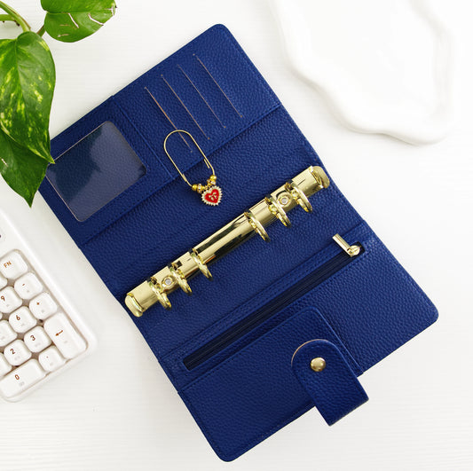 Blue leather binder with gold hardware on a white surface with a plant and calculator.