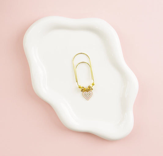 Gold paper clip with heart detail on a white dish against a pink background