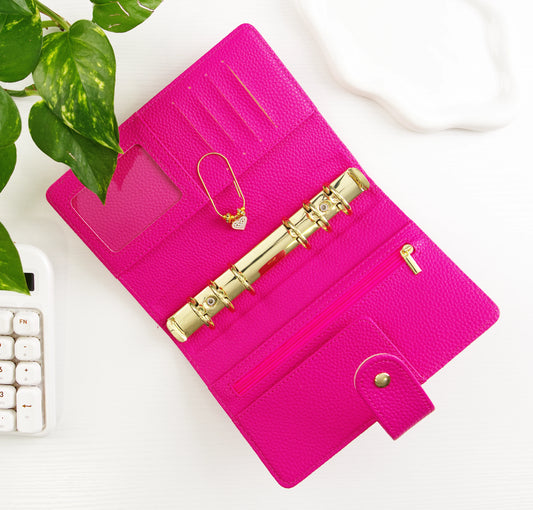 Pink binder with gold accents on a white surface with a plant in the corner